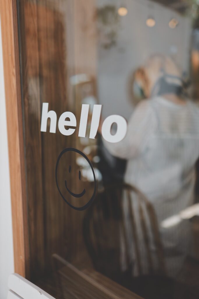 Close-up of a glass window with 'hello' and smiley face sticker reflecting an indoor scene.
